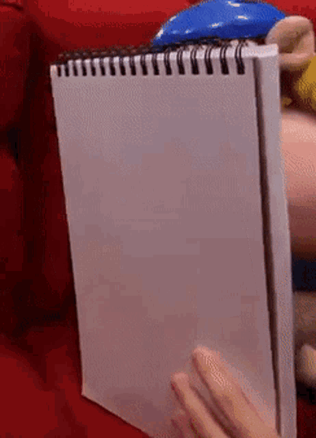 a person is holding a white spiral bound notebook on a red couch