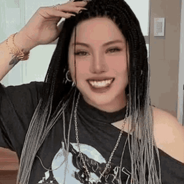 a woman with braids and a necklace is smiling and holding her hair .