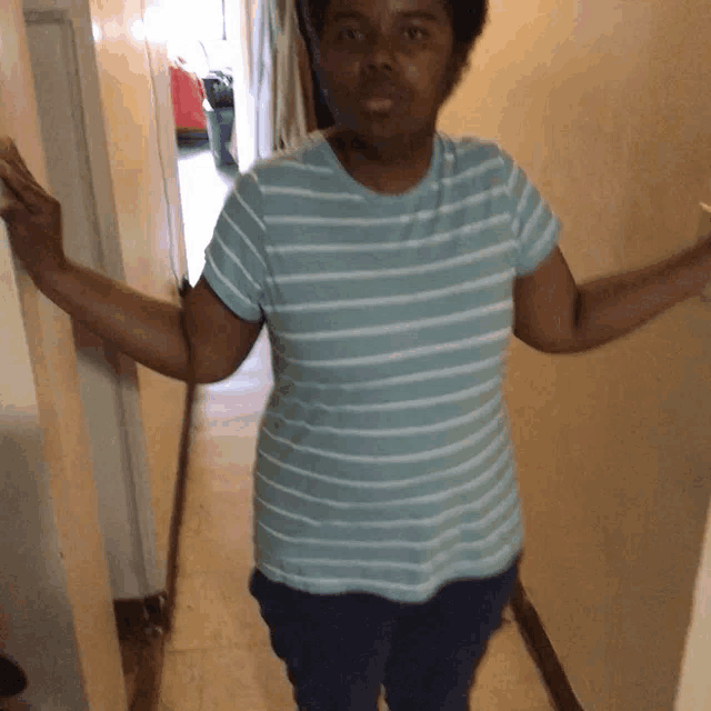 a woman wearing a blue and white striped shirt stands in a hallway