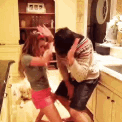 a man and woman are dancing in a kitchen with a dog in the background