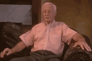 an elderly man in a pink shirt is sitting on a couch with his arms outstretched .