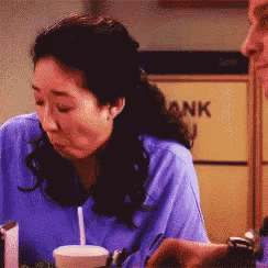 a woman in a blue scrub top is sitting at a table in front of a yellow cabinet that says bank