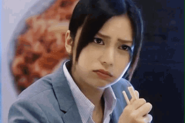 a woman in a suit and striped shirt is eating with chopsticks