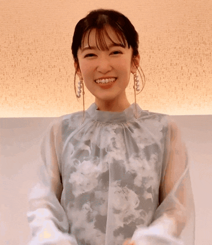 a woman wearing a floral top and earrings smiles