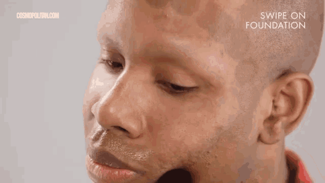 a man with a bald head is applying makeup to his face .
