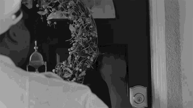 a black and white photo of a person knocking on a door with a wreath on it