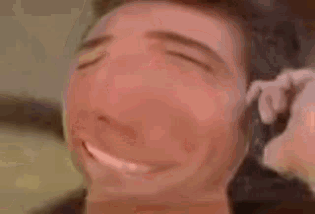 a man is laying on a bed with his eyes closed and a gun in his ear .