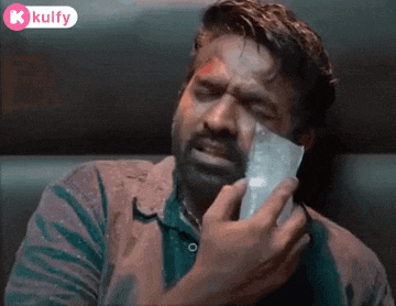 a man is holding a piece of paper in his hand and crying while talking on a cell phone .