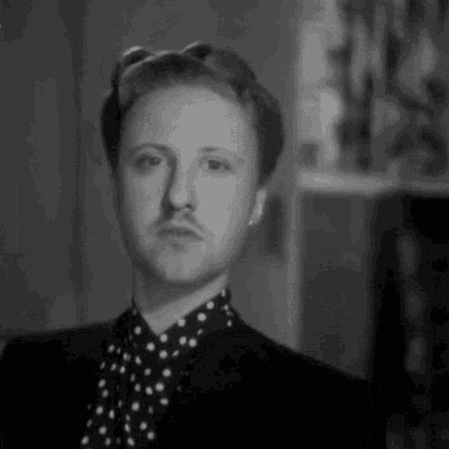 a man with a mustache is wearing a polka dot shirt and a black jacket .