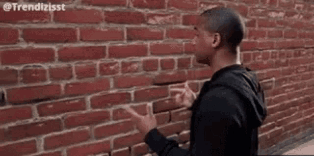 a man is standing in front of a brick wall and looking at it .