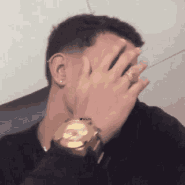 a man wearing a gold watch and a ring is covering his face with his hand .
