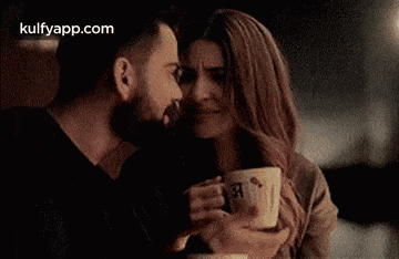 a man and a woman are holding cups of coffee and kissing .