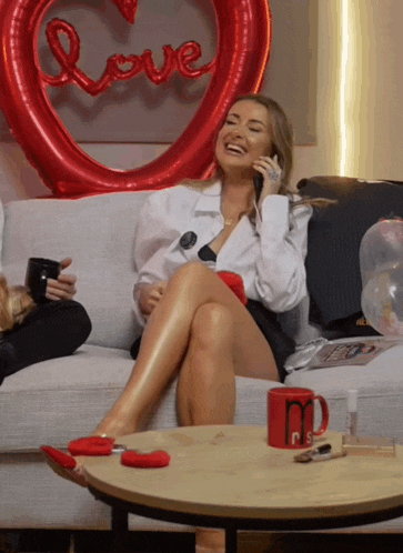 a woman sits on a couch with her legs crossed talking on a phone