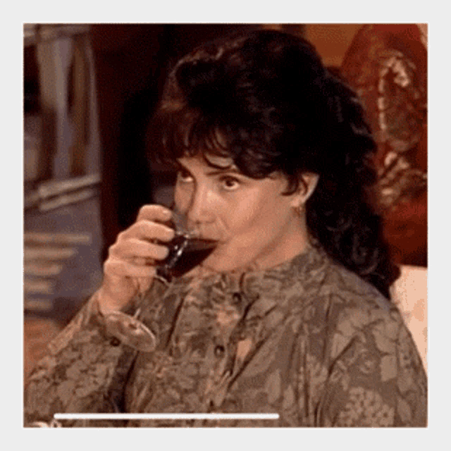 a woman is drinking a glass of wine and looking at the camera