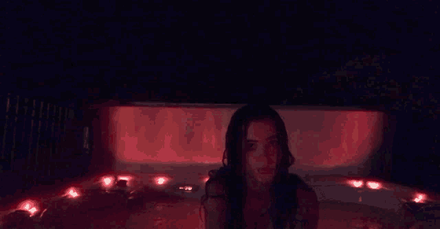 a woman is sitting in a hot tub at night with red lights on