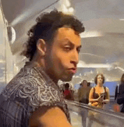 a man with a mohawk is standing in front of a crowd of people in an airport .