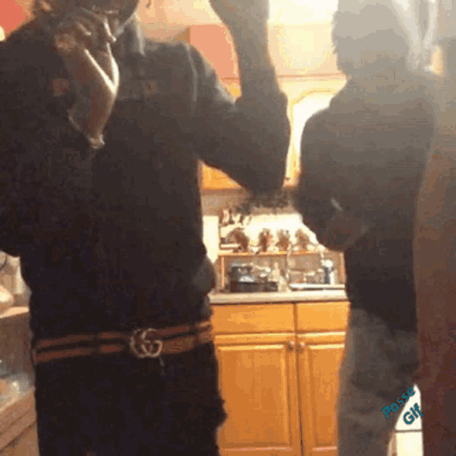 a man in a black shirt with a gucci belt stands in a kitchen
