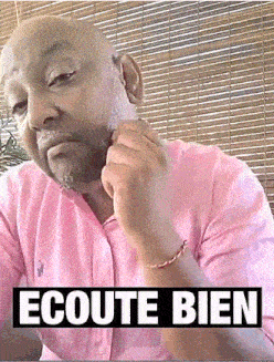a man in a pink shirt is sitting in front of a bamboo blind with the words ecoute bien on the bottom