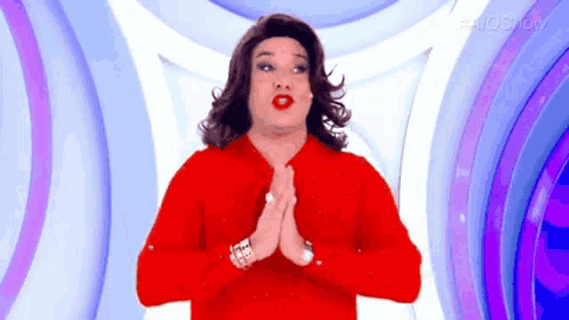 a man in a red shirt and wig is praying with his hands folded .