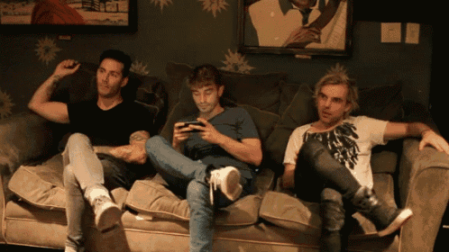 three men are sitting on a couch and one of them is looking at his phone