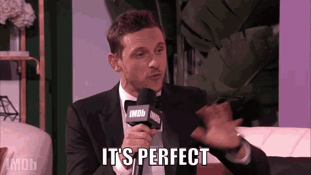 a man in a tuxedo is holding a microphone and says it 's perfect