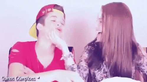 a girl is touching a boy 's face and the words somos cumplices are on the bottom of the image