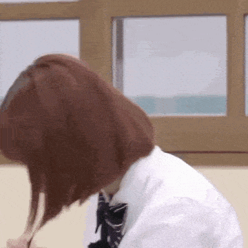 a girl in a school uniform is sitting at a desk in front of a window in a classroom .