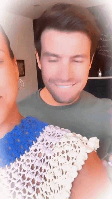 a man with his eyes closed smiles while holding a woman 's arm