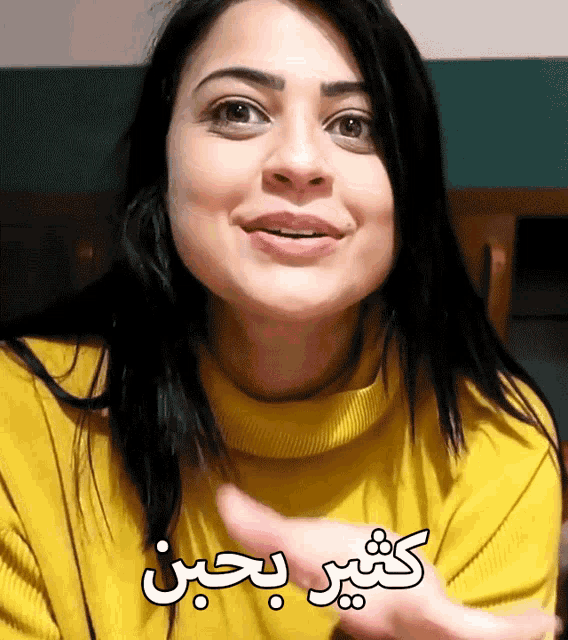 a woman wearing a yellow sweater is smiling with arabic writing above her
