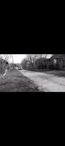 a black and white photo of a street with a car driving down it .