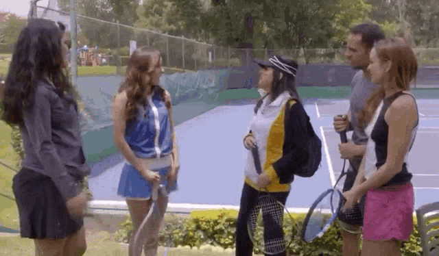 a group of people are standing on a tennis court talking to each other .