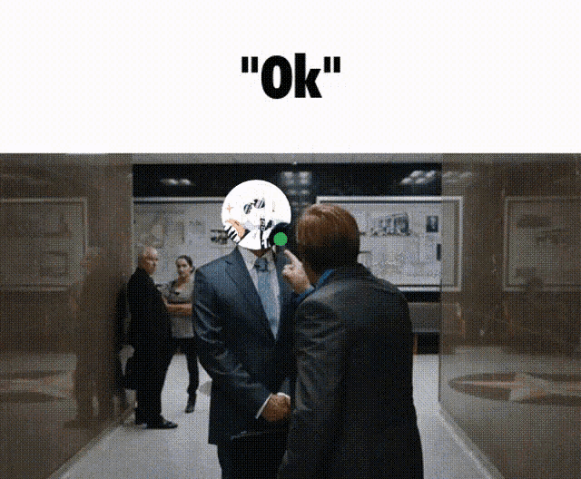 a man in a suit is shaking hands with another man with a mask on his head that says " ok " on it