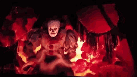 a clown in a mask is standing in a dark room surrounded by fire and smoke .