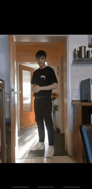 a young man standing in a hallway wearing a black stussy shirt