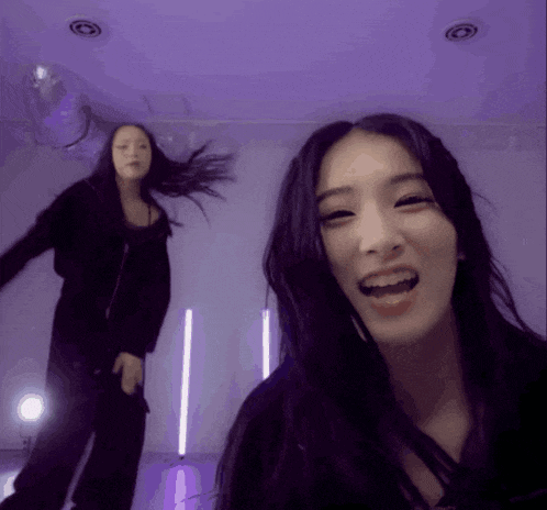 two women are dancing in a room with purple lights behind them