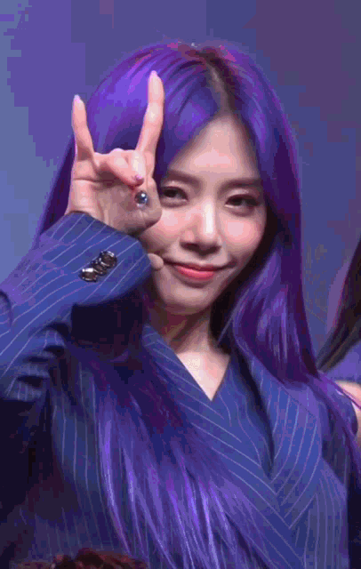 a woman with purple hair is wearing a blue suit and giving a peace sign