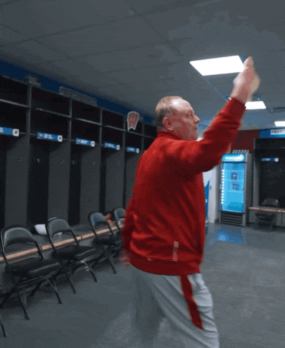 a man in a red jacket is dancing in a locker room with the number 2 on the wall