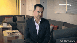 a man in a suit is sitting in a living room with a gifrun.com watermark