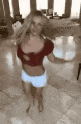 a woman is dancing in a living room while wearing shorts and a red top .
