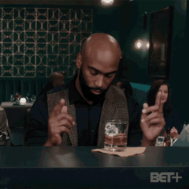 a man sitting at a bar with a glass of whiskey and a napkin that says bet + on it