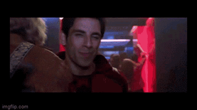 a man with blonde hair is standing in front of a group of people in a club .