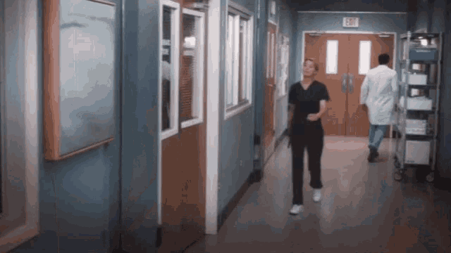 a nurse is walking down a hospital hallway with a doctor behind her .