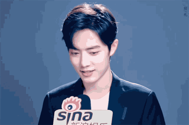 a man in a suit stands in front of a microphone that says sina