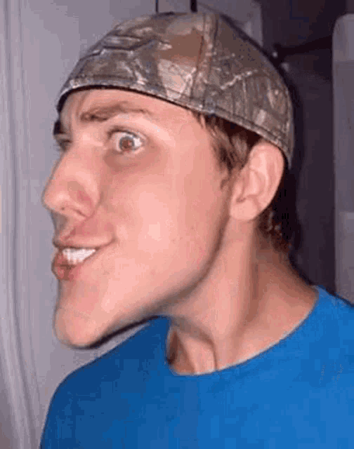 a man wearing a blue shirt and a hat is making a funny face .