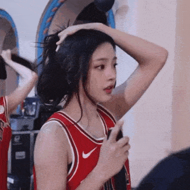a woman in a red basketball jersey is holding her hair in a bun .
