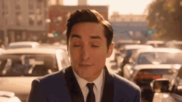 a man in a suit and tie is standing in front of a busy street with his eyes closed .