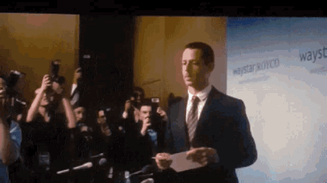 a man in a suit and tie is standing in front of a sign that says waystar