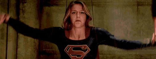 a woman in a superman costume is standing in front of a wall and talking to a man .