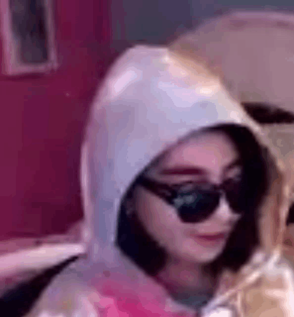 a woman wearing sunglasses and a hoodie is looking at her phone .