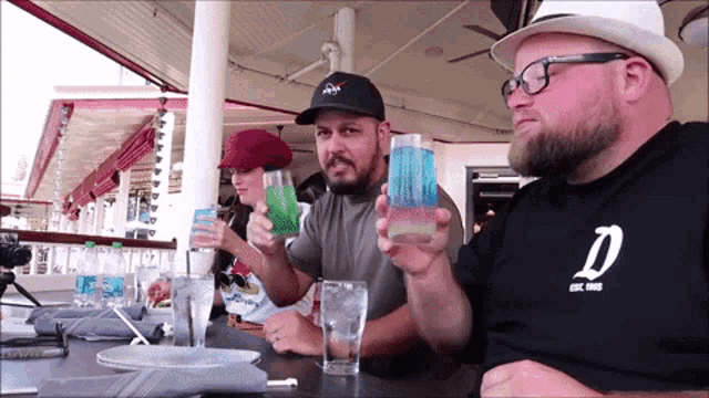 a man wearing a nasa hat sits at a table holding a drink